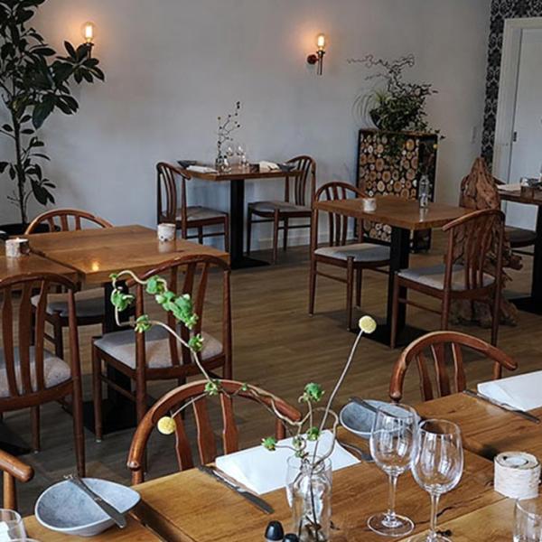 Stemningsfuld spisestue på Sdr. Omme Kro med dækkede træborde, klassiske træstole og grønne dekorationer. En af spiseoplevelserne på Small Wonders-ruterne.