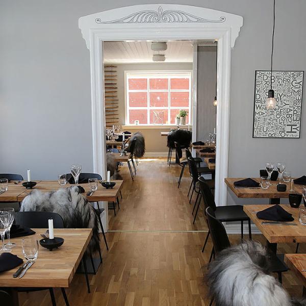 Lyst og moderne restaurantmiljø hos Spiseriet i Billund med dækkede træborde, sorte stole og hyggelige detaljer. En del af spiseoplevelserne på Small Wonders-ruterne.