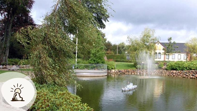 Vorbasse bypark med sø, vandfontæne og små huse i baggrunden. Vorbasse er en del af Kunstruten i Small Wonders – Heart of Jutland.