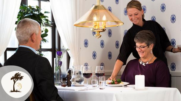 Gæster nyder middag på Filskov Kro, hvor en tjener serverer ved bordet. Kroen er en del af Small Wonders-ruten.