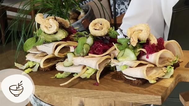 Smørrebrød fra Sdr. Omme Kro anrettet på træbræt med kød, friske grøntsager, sprøde toppings og urter. Kroen er en del af Gastroruten i Small Wonders.