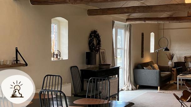 Lyst og hyggeligt loungeområde hos Bolding Apartments med sofaer, spiseplads og træbjælker. Et af overnatningsstederne på Kunstruten i Small Wonders – Heart of Jutland.