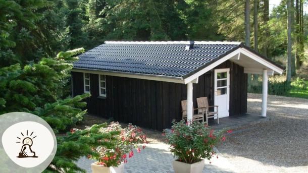 Lille sort træhytte med terrasse og natur omkring hos Gregersminde, et af overnatningsstederne på Kunstruten i Small Wonders – Heart of Jutland.