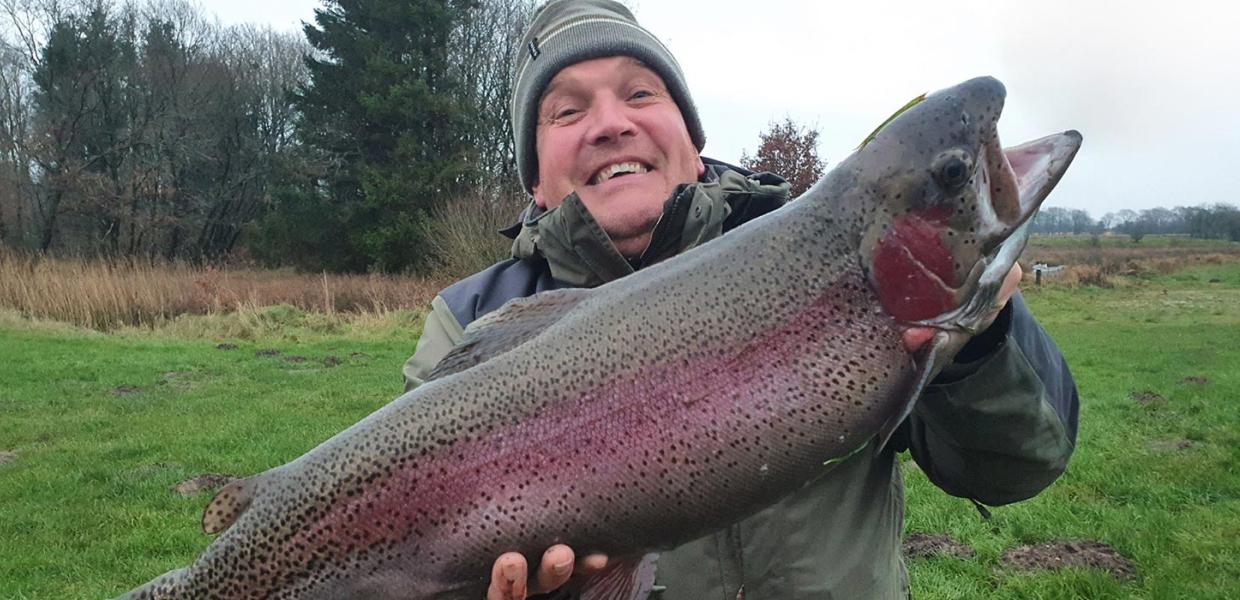 Person holder en stor regnbueørred fanget ved Filskov Fiskesø, et stop på Gastroruten i Small Wonders.