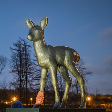 Skulpturen Råbarn i Skulpturpark Billund, vist i aftenlys med træer og parkens lamper i baggrunden. En del af Kunstruten i Small Wonders – Heart of Jutland.