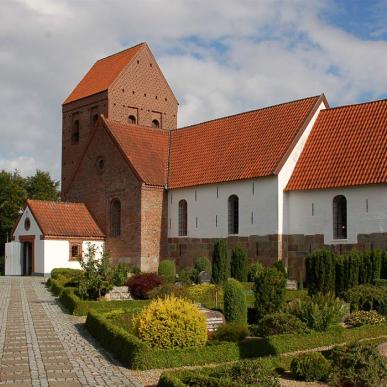 orbasse Kirke set udefra med hvidkalkede mure, rødt tegltag og omgivende kirkegård. Kirken er et stop på Kunstruten i Small Wonders – Heart of Jutland.