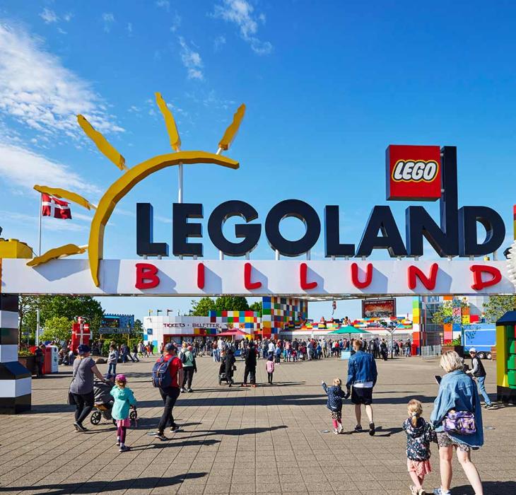 Portalen til LEGOLAND med de to tårne af LEGO® klodser. En masse gæster er på ind for at hygge sig i parken på en sommerdag under en blå himmel.